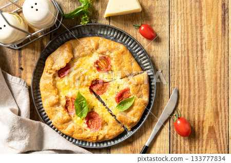 Crispy tomato galette with adyghe cheese and herbs on rustic background. Top view. Crispy tomato galette with adyghe cheese and herbs on rustic background. Top view. 133777834