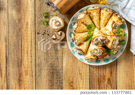 Crispy lavash rolls with mushroom filling, cheese and herbs on a rustic wooden table. Top view. Crispy lavash rolls with mushroom filling, cheese and herbs on a rustic wooden table. Top view. 133777861