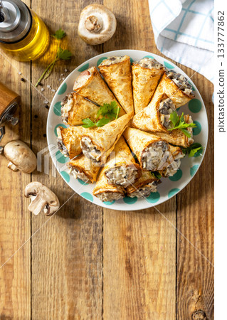 Crispy lavash rolls with mushroom filling, cheese and herbs on a rustic wooden table. Top view. 133777862