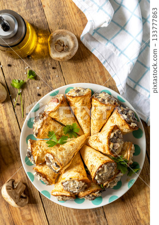 Crispy lavash rolls with mushroom filling, cheese and herbs on a rustic wooden table. Top view. 133777863