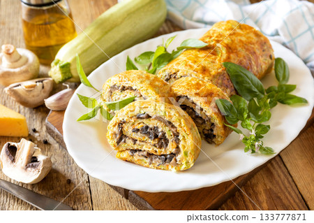 Zucchini roll with mushroom filling and herbs served on a white plate on a rustic table. Zucchini roll with mushroom filling and herbs served on a white plate on a rustic table. 133777871