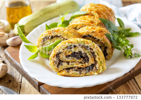 Zucchini roll with mushroom filling and herbs served on a white plate on a rustic table. Zucchini roll with mushroom filling and herbs served on a white plate on a rustic table. 133777872