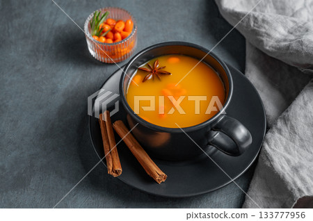 Sea buckthorn tea in a black cup on a dark background with berries, spices and napkin. 133777956