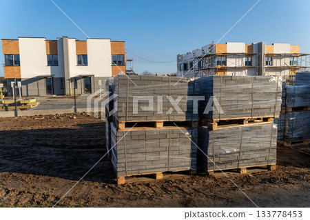 Pallets of gray paving stones wrapped in plastic on a dirt ground Pallets of gray paving stones wrapped in plastic on a dirt ground 133778453