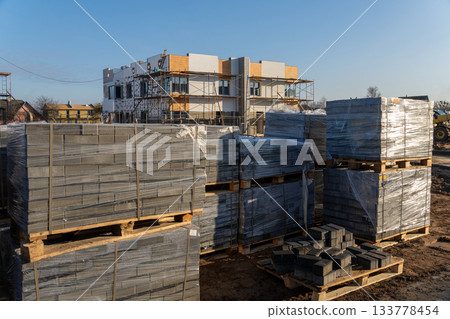 Pallets of gray paving stones wrapped in plastic on a dirt ground 133778454