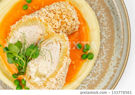 Crispy chicken roll served on creamy mashed potatoes with vibrant carrot pure and fresh green peas, top view 133778561