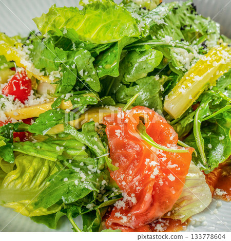 Fresh green salad with leafy greens, cherry tomatoes, smoked salmon and grated cheese in vibrant close-up ideal for healthy food advertising and menu design Fresh green salad with leafy greens, cherry tomatoes, smoked salmon and grated cheese in vibrant close-up ideal for healthy food advertising and menu design 133778604