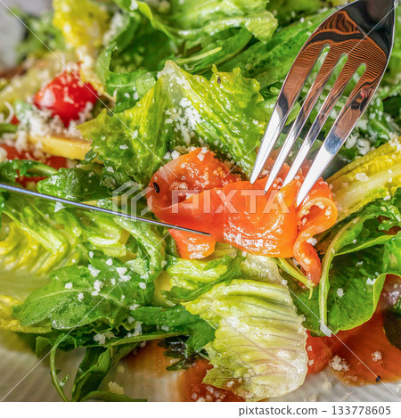 Fresh green salad with smoked salmon, crisp lettuce and grated cheese in a vibrant macro shot with fork, perfect for healthy food advertising and restaurant menus 133778605