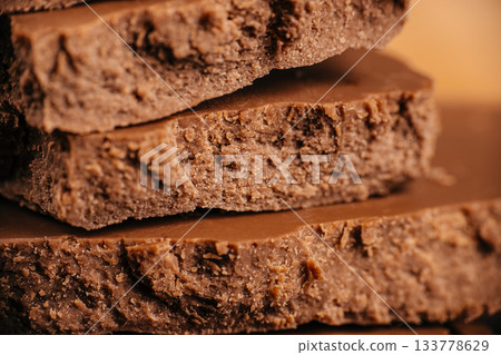 Macro texture of layered porous milk chocolate with rough aerated structure and warm lighting, ideal for confectionery advertising, packaging design and gourmet sweet food visuals 133778629