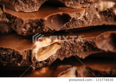 Macro texture of broken milk chocolate with whole hazelnuts, layered in a warm close-up composition, ideal for premium confectionery advertising, dessert branding, packaging design 133778630