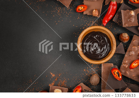 Dark chocolate cream in a wooden bowl with chili peppers, hazelnuts and assorted chocolate pieces on black background copy space, dessert advertising and spicy chocolate concepts Dark chocolate cream in a wooden bowl with chili peppers, hazelnuts and assorted chocolate pieces on black background copy space, dessert advertising and spicy chocolate concepts 133778633