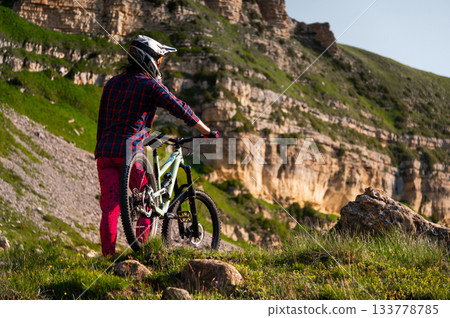 Man riding a mountain bike on a dirt road for an adrenaline rush, fitness, or extreme outdoor sport. A man cyclist or biker riding for stunts 133778785