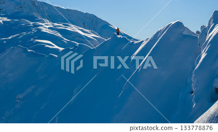 Aerial photo of a ski mountaineer standing on a snowy alpine ridge in Austria. Winter landscape, backcountry adventure, clear blue sky with sunshine and solitude in breathtaking mountain scenery. 133778876