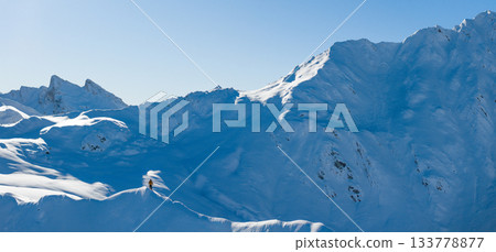 Aerial photo of a ski mountaineer standing on a snowy alpine ridge in Austria. Winter landscape, backcountry adventure, clear blue sky with sunshine and solitude in breathtaking mountain scenery. 133778877