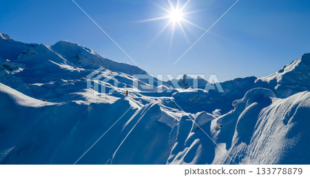 Aerial photo of a ski mountaineer standing on a snowy alpine ridge in Austria. Winter landscape, backcountry adventure, clear blue sky with sunshine and solitude in breathtaking mountain scenery. 133778879