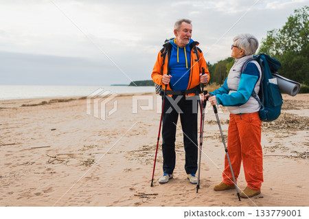 Hiking tourism adventure. Senior couple man woman enjoying outdoor recreation hiking on beach. Happy old people backpackers hikers enjoy walking hike trekking tourism active vacation beauty of nature Hiking tourism adventure. Senior couple man woman enjoying outdoor recreation hiking on beach. Happy old people backpackers hikers enjoy walking hike trekking tourism active vacation beauty of nature 133779001