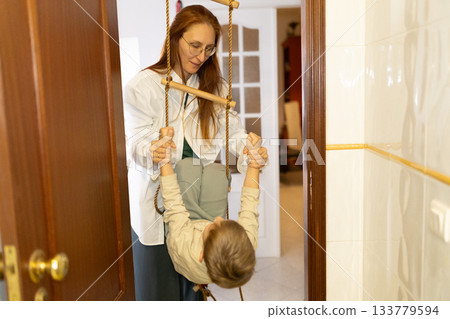 Mother helping child playing on indoor rope ladder 133779594
