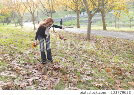 Woman collecting autumn leaves in park during autumn season 133779628