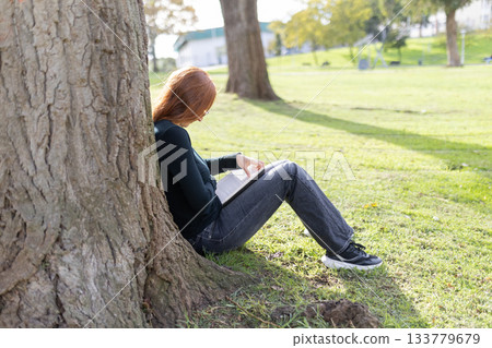 Woman reading book relaxing in park on sunny day 133779679