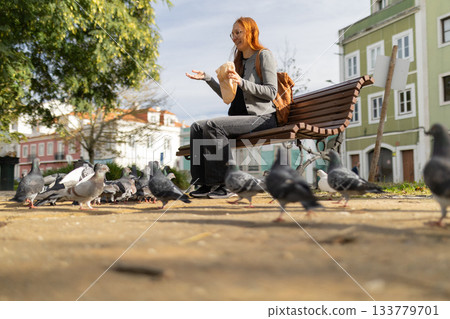 Young woman feeding pigeons in city park Young woman feeding pigeons in city park 133779701