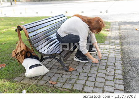 Woman clearing weeds from cobblestone path in park Woman clearing weeds from cobblestone path in park 133779708