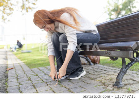 Woman tying shoelace sitting on park bench Woman tying shoelace sitting on park bench 133779713