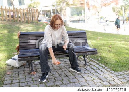 Woman opening box with utility knife on park bench Woman opening box with utility knife on park bench 133779716