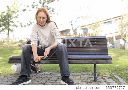 Woman holding multi tool sitting on a park bench 133779717
