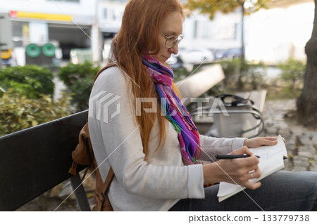 Woman sketching in notebook on a park bench Woman sketching in notebook on a park bench 133779738