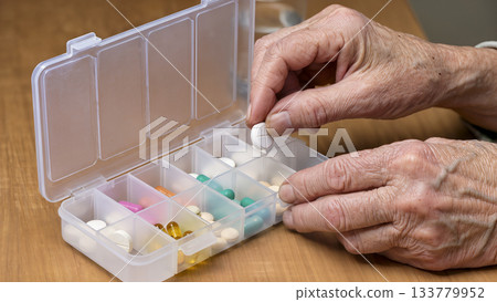 Hands of an elderly person taking a pill from a weekly pill organizer (pill box). 133779952