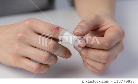 First aid: hands applying a medical bandage or patch to a finger with a small wound or cut. 133779953