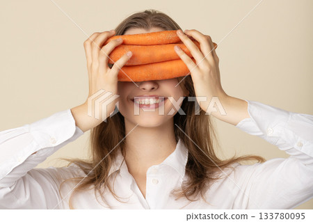 Woman covering her eyes with orange carrots and smiling 133780095