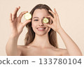 Beautiful young woman covering her eye with cucumber slices 133780104