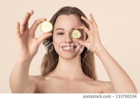 Beautiful young woman covering her eye with cucumber slices 133780104