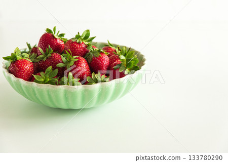 Fresh red strawberries in a green bowl on white table. Front view 133780290