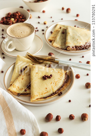 Crepes with chocolate hazelnut spread, strawberries and hazelnuts on a white wooden table. Top view 133780291