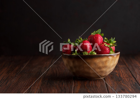 Fresh red strawberries in a rustic bowl on a dark wooden background. Front view 133780294