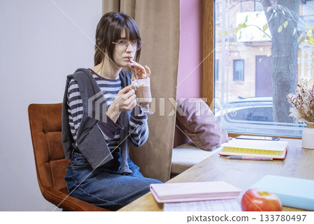 Young woman reading a book in a cozy cafe with a cup of cocoa. Young woman reading a book in a cozy cafe with a cup of cocoa. 133780497