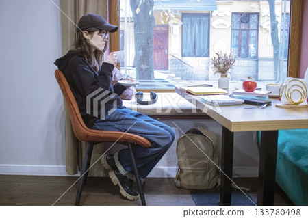Young woman reading a book in a cozy cafe with a cup of cocoa. 133780498