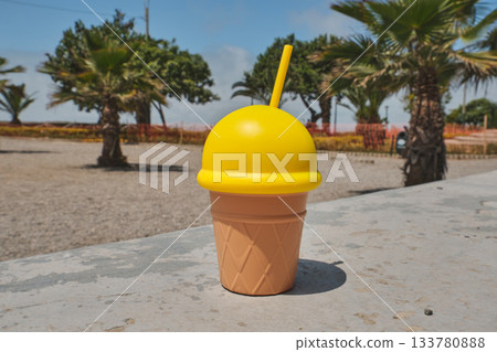 Yellow ice cream cup with straw on a summer day 133780888