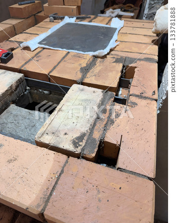 Installation of the cooking plate for a heating stove. Brickwork during the construction of a heating stove. Installation of the cooking plate for a heating stove. Brickwork during the construction of a heating stove. 133781888