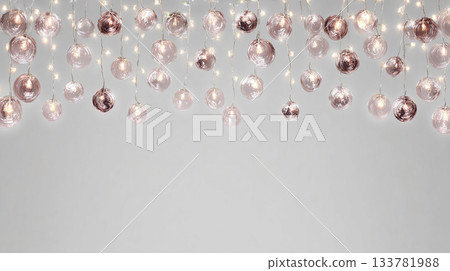 festive string lights hanging from the ceiling, casting a soft glow on clear glass marbles in shades of rose gold and white against an isolated gray background 133781988