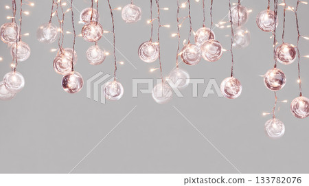 festive string lights hanging from the ceiling, casting a soft glow on clear glass marbles in shades of rose gold and white against an isolated gray background 133782076