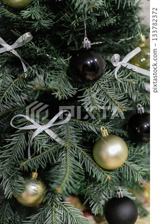 Close up of a tree branch with white bows and gold Christmas ornaments 133782372