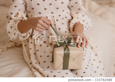 Caucasian child hands opening gift box on beige bed in cozy room Caucasian child hands opening gift box on beige bed in cozy room 133782986