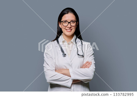 Portrait of smiling female doctor in white lab coat with stethoscope on gray background Portrait of smiling female doctor in white lab coat with stethoscope on gray background 133782995