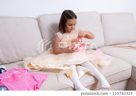 Young caucasian girl unwrapping gift on couch in pink dress Young caucasian girl unwrapping gift on couch in pink dress 133783323