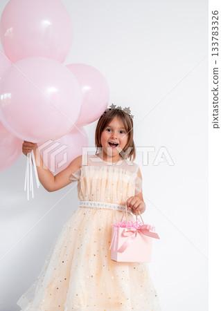 Caucasian young girl in party dress holding pink balloons and gift Caucasian young girl in party dress holding pink balloons and gift 133783326