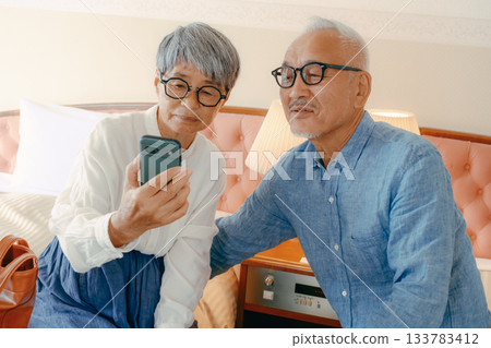 Senior couple talking while looking at smartphone at hotel 133783412