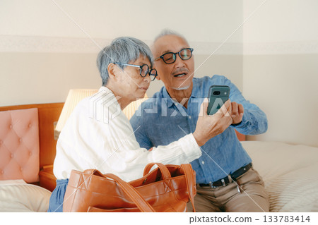 Senior couple talking while looking at smartphone at hotel 133783414